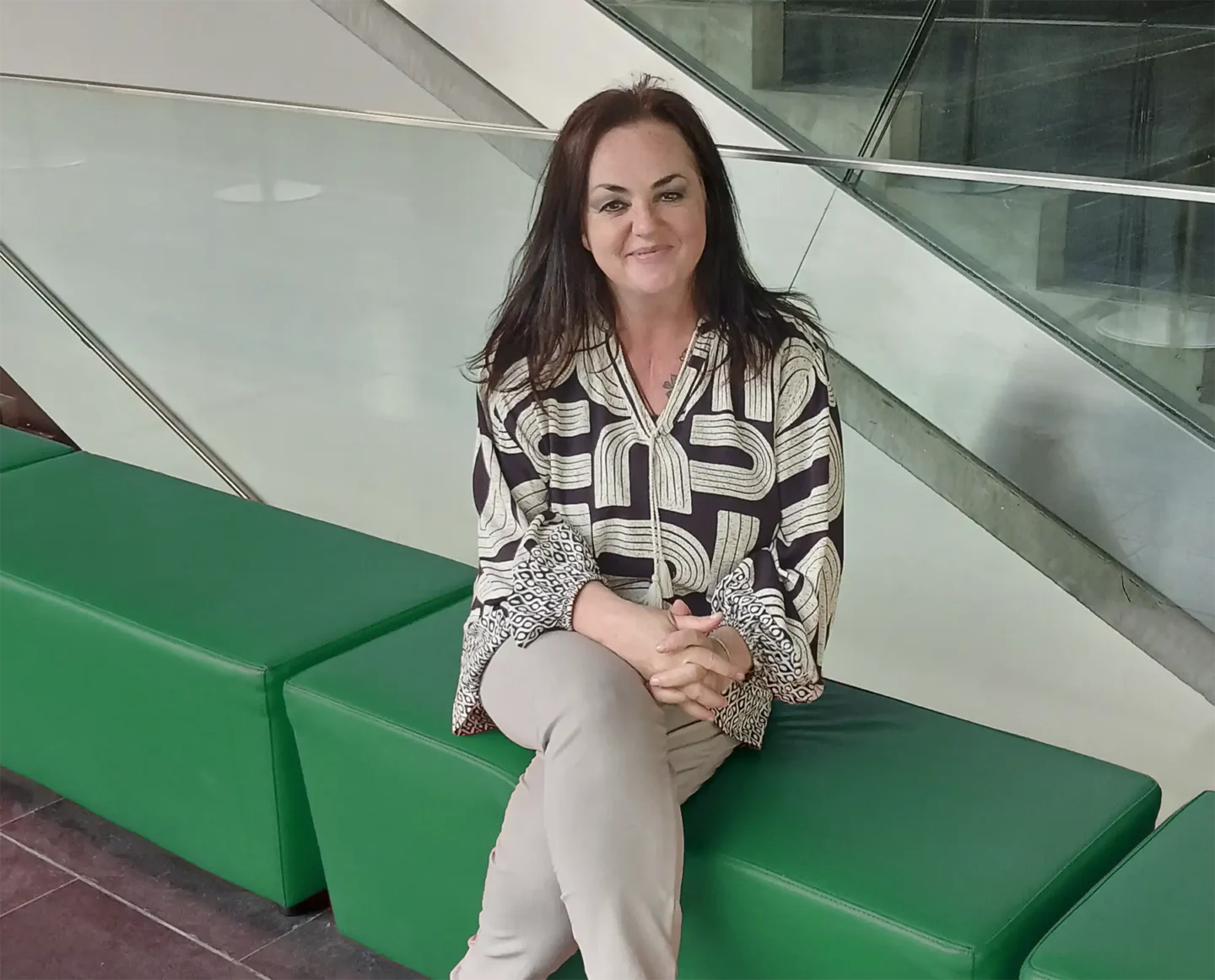 Renate Hofer sitzt auf einer grünen Bank und lächelt in die Kamera